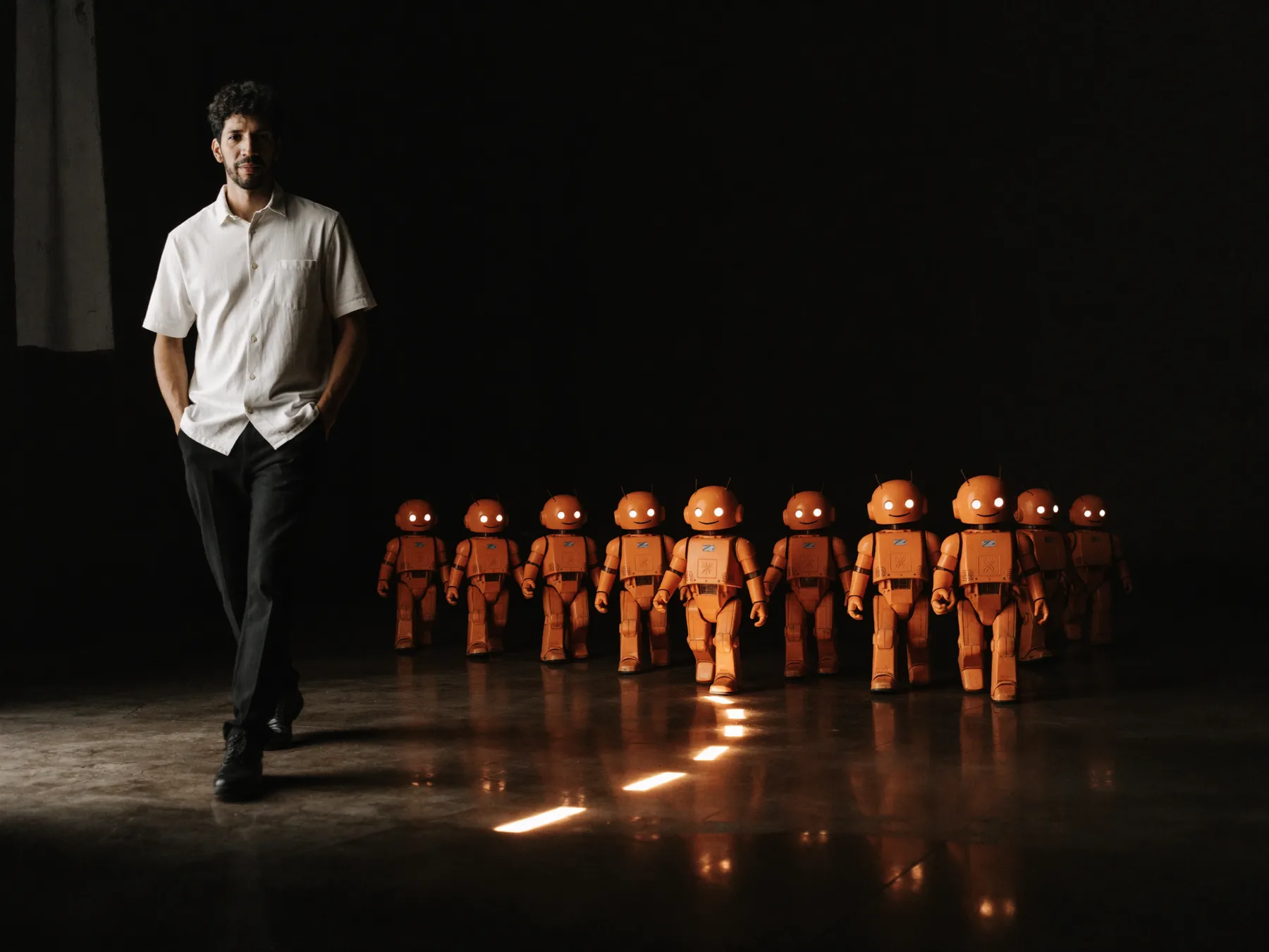 Thales Laray caminhando à frente de uma fileira de robôs laranja